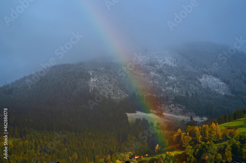 beautiful rainbow over the fresh snowcapped mountains and green fields at a autumn morning