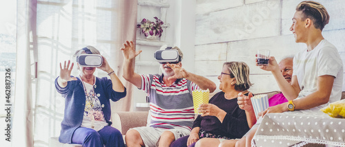 Group of mixed ages people have fun all together during celebration - senior grandfathers and grandson boy laugh a lot using goggles vr technology to play and have fun indoor at home photo