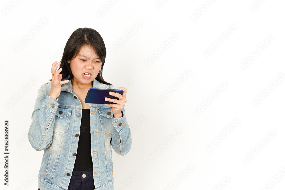 Playing Game on Phone With Angry Face of Beautiful Asian Woman Wearing Jeans Jacket and black shirt Isolated On White Background Playing Game on Phone With Angry Face of Beautiful Asian Woman Wearing Jeans Jacket and black shirt Isolated On White Background