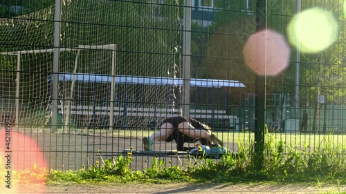 a girl does exercises at the stadium, Does the exercise movement of the legs to the left and right Black tracksuit. View from the back. A stadium with a grid. Beautiful evening light. Glare from the s photo