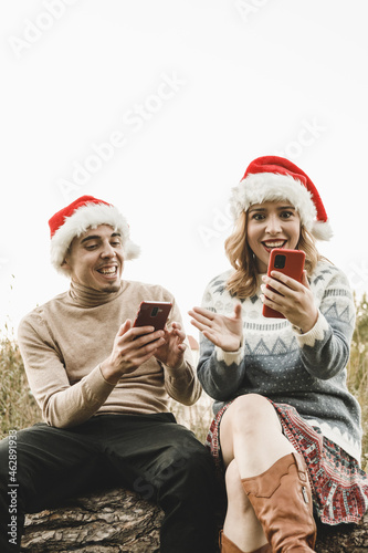 Hispanic couple in Santa hats are using smartphones, outdoors
