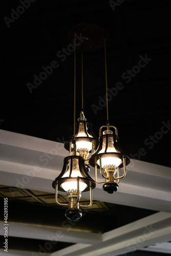 A luxury celing lighting lamp is glowing in warm light shade, with beam structure and dark area as background. Interior decoration furniture object photo. Close-up and selective focus. photo