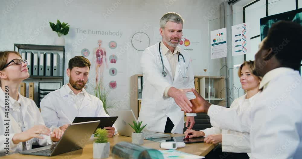 Workflow in medical office where handsome confident qualified bearded doctor greeting every member of his multiethnic team with handshakes before the start of joint conference Workflow in medical office where handsome confident qualified bearded doctor greeting every member of his multiethnic team with handshakes before the start of joint conference