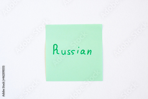 Top view flat lay of the reminder notepaper of green color with word Russian on it on white background. Flashcards and language studies concept