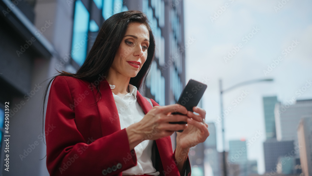 Portrait of Multiethnic Adult Businesswoman Using Smartphone on Street in a Big City. Confident Manager Connecting with People Online, Messaging, Browsing Internet on Her Way to Office. Low Angle Shot