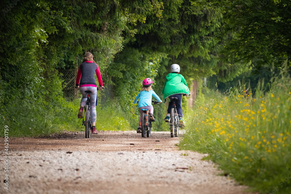 Mother, a son, and a preschool daughter cycling on a gravel road near the forest