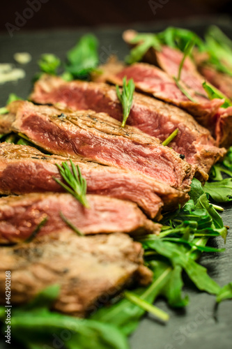 Close up of Sliced beef meat, medium rare grilled, with rosemary and rocket salad on a plate