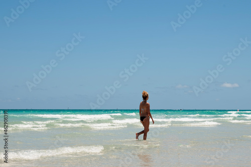 A woman with a fit body, wearing bikini walking on Miami beach on a summer day with a cloudless sky © Marco B.
