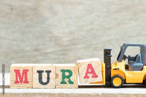 Toy forklift hold letter block a to complete word mura on wood background
