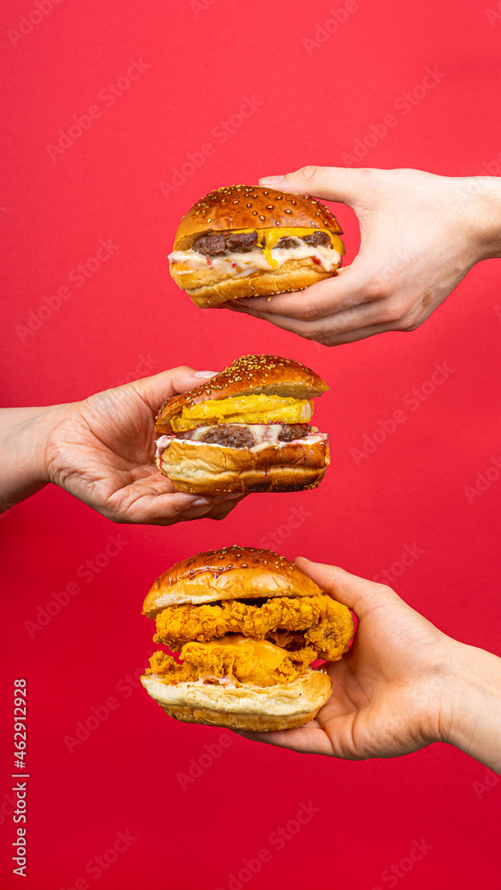 three human hands holding tasty hamburgers cheeseburger burger isolated on red background three human hands holding tasty hamburgers cheeseburger burger isolated on red background