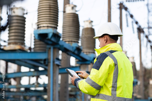 Electrical engineer studying reading on tablet. Electrical worker engineer a working with digital tablet, power near tower with electricity. Energy business technology industry concept photo