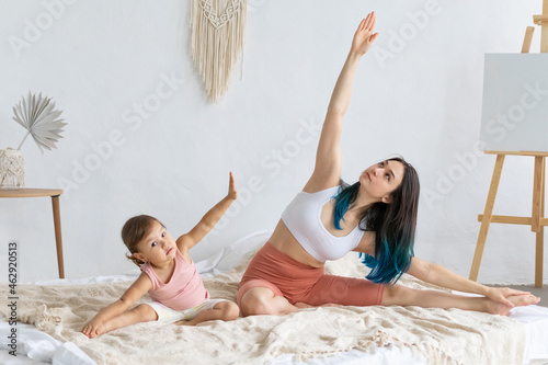 Young woman practices yoga on the bed with her little daughter.Couples yoga. photo