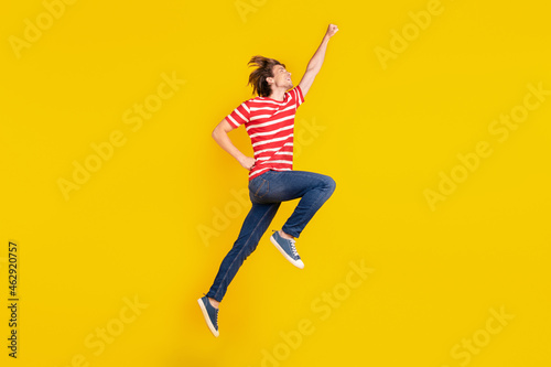 Photo of cute strong young man wear striped t-shirt jumping high looking empty space isolated yellow color background