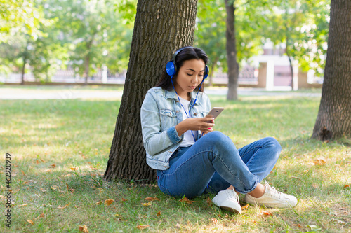 Portrait of an Asian woman in headphones with smartphone. She smiles and listens to her favorite music.