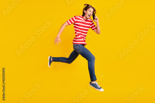 Photo of impressed cute man wear striped t-shirt running talking modern device looking empty space isolated yellow color background