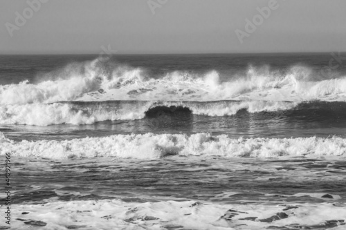Imagen horizontal en blanco y negro del mar y las olas rompiendo en la playa.