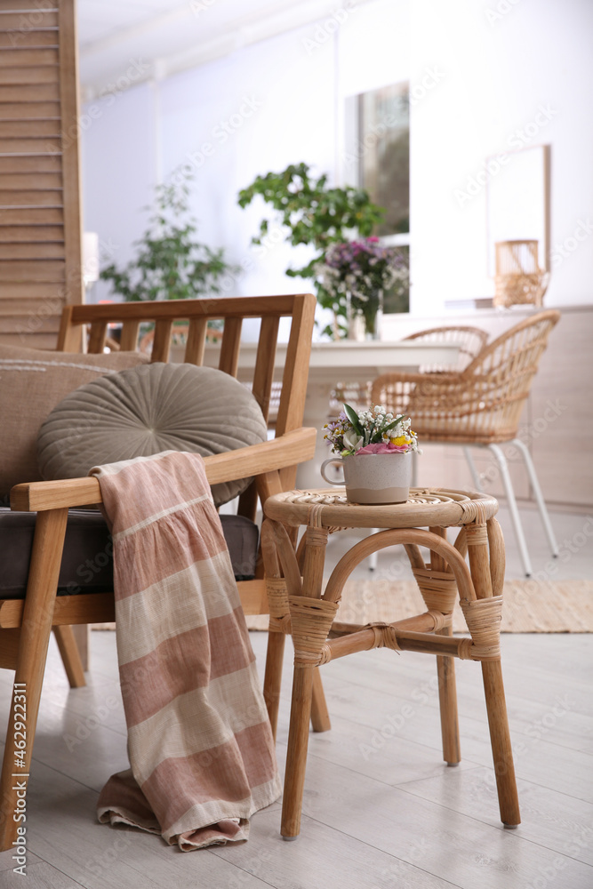 Stylish wooden stool with bouquet of flowers near armchair in room. Interior element