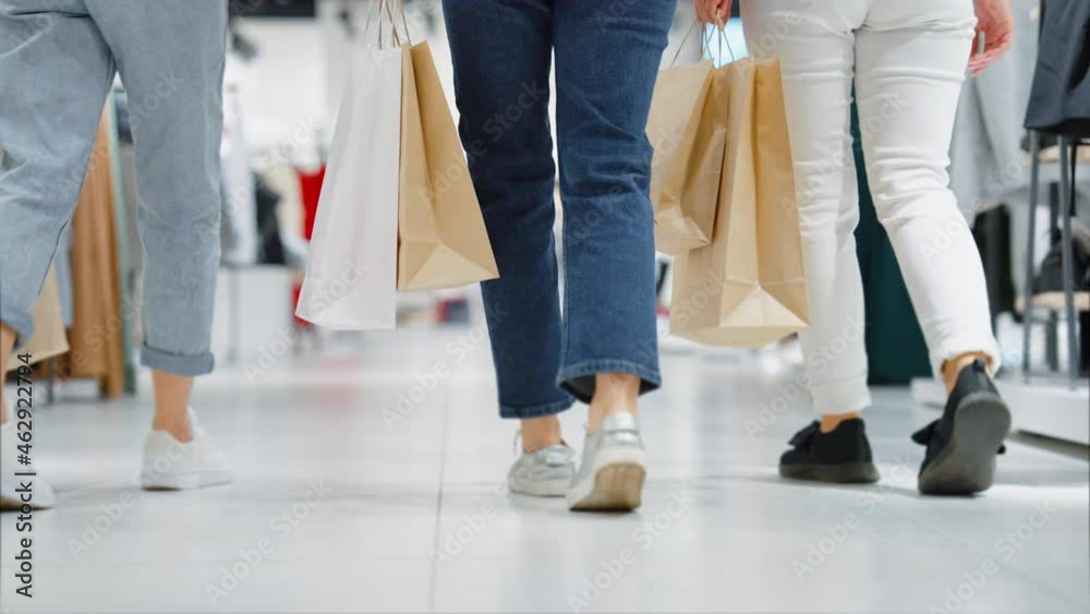 Female legs in jeans of different color walking in mall in slow motion. Following shot of women carrying shopping bags. Friends spending time together. Concept of shopping