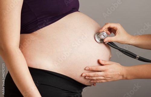 pregnant woman being examined by doctor on gray studio background, stethoscope on belly,health care concept