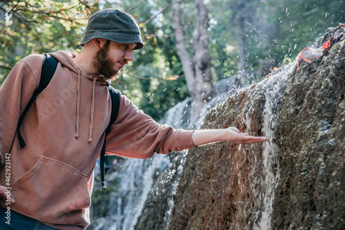 Φωτογραφία Joven barbudo con un sombrero de pescador tocando el agua que corre por la pared