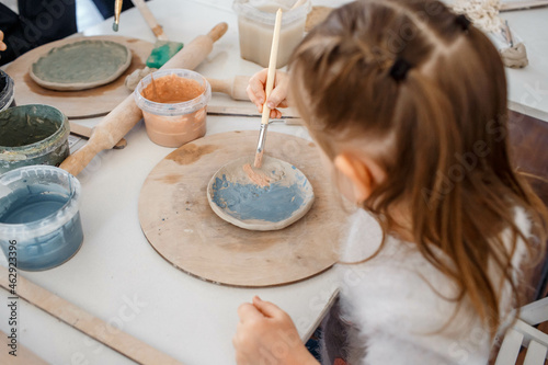 Child working on pottery wheel. Kids arts and crafts class in workshop. Little girl creating cup and bowl of clay. Creative activity in school.