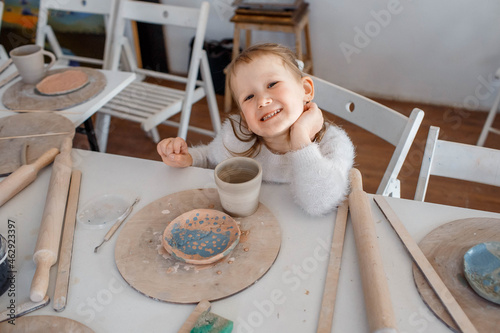 Child working on pottery wheel. Kids arts and crafts class in workshop. Little girl creating cup and bowl of clay. Creative activity in school.