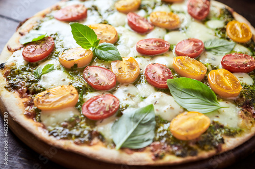 Pizza with cherry tomatoes, mozzarella and basil pesto. Dark wooden background. Close up. 
