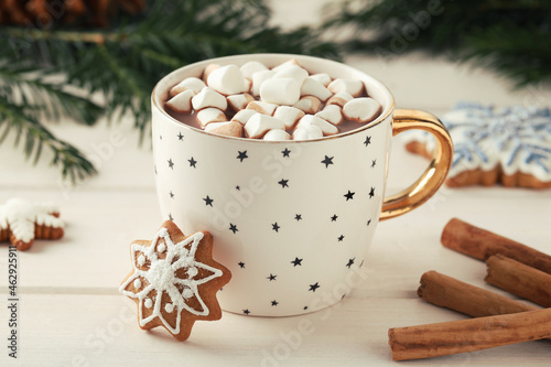 Delicious hot chocolate with marshmallows, gingerbread cookies and cinnamon on white wooden table, closeup photo