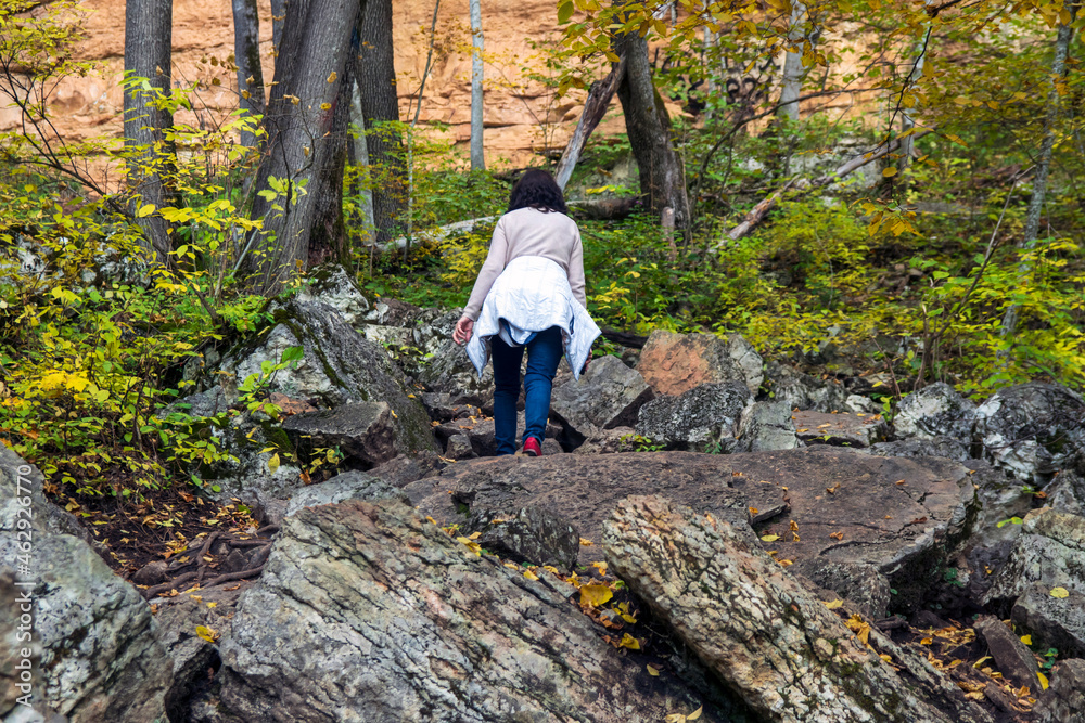 Rear view of a woman walking along a path in the forest and overcoming huge stones.