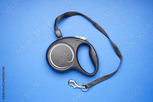 Black retractable dog leash on a blue background, flat lay.