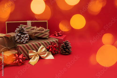 Winter holidays decoration. wrapped Christmas gifts, fir cones with bokeh lights on red background. Selective focus.