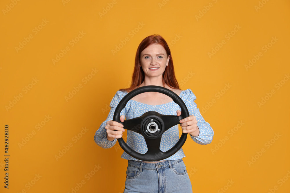 Fototapeta premium Happy young woman with steering wheel on yellow background