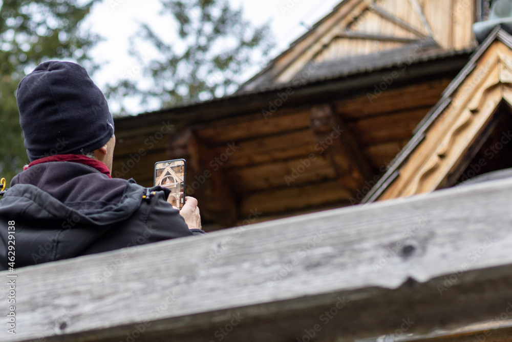 Man is taking a photo of rural house by smartphone. Chapel of Of the Sacred Heart of Jesus in Jaszczurówka. Jaszczurowka.