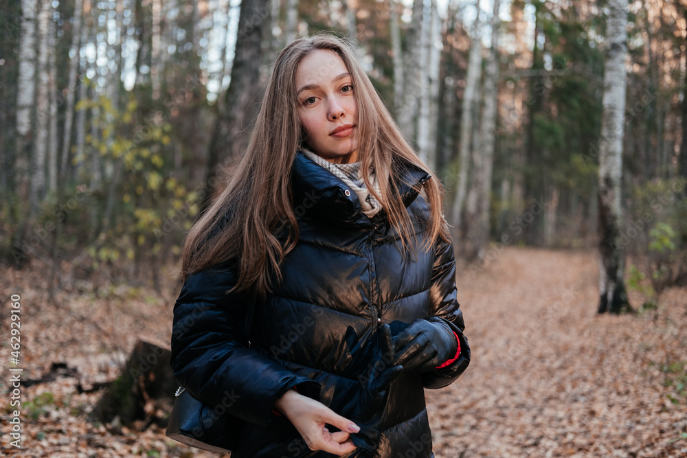 Smiling young woman in coat and scarf standing in autumn forest. Woman looking at the sunset on trees background and breathing fresh air. Person in nature. Having fun outdoors. Smiling young woman in coat and scarf standing in autumn forest. Woman looking at the sunset on trees background and breathing fresh air. Person in nature. Having fun outdoors.