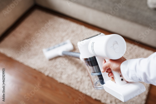 Fotografía Powerful cordless vacuum cleaner with white cyclonic dust collection technology in hand, cleans the carpet in the house near the sofa