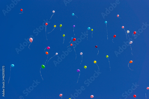 Bright inflatable balloons fly in the air against the backdrop of trees and blue sky during a festive holiday. Fireworks in the sky from colorful balloons.