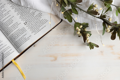 Open bible with Christmas sprig with white berries with lights on a white wood background with copy space