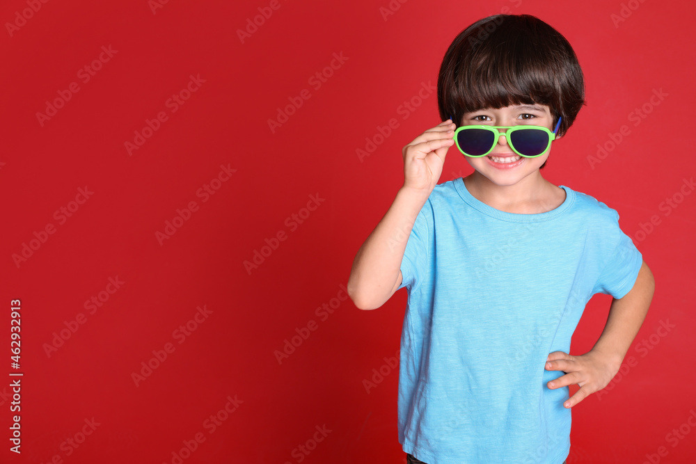 Cute little boy with sunglasses on red background, space for text