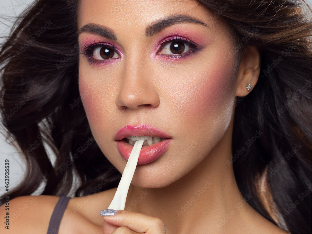 Beautiful close-up portrait of a girl with long curly hair and evening pink makeup. The girl pulls the gum out of her mouth. Extremely long eyelashes and gentle facial skin care Beautiful close-up portrait of a girl with long curly hair and evening pink makeup. The girl pulls the gum out of her mouth. Extremely long eyelashes and gentle facial skin care