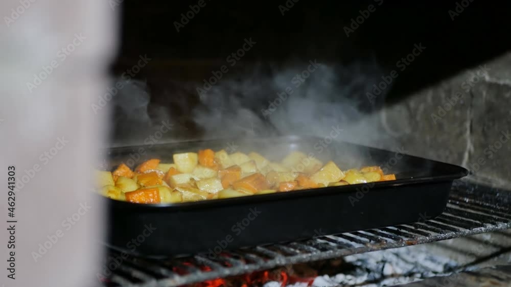 In a brick oven, vegetables are cooked in a baking sheet on a metal wire rack. Hot food emits steam due to the cool air temperature. Family dinner outdoors in the evening In a brick oven, vegetables are cooked in a baking sheet on a metal wire rack. Hot food emits steam due to the cool air temperature. Family dinner outdoors in the evening