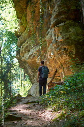 An adult backpacker walking around a cave in a forest on a sunny day