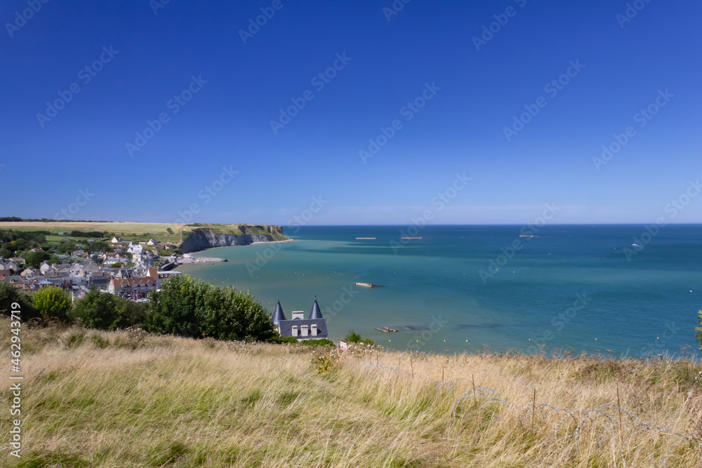 view on Arromanches bay in Normandy France. Blue sky and water and visible remains of the world war mulberry harbour elements.