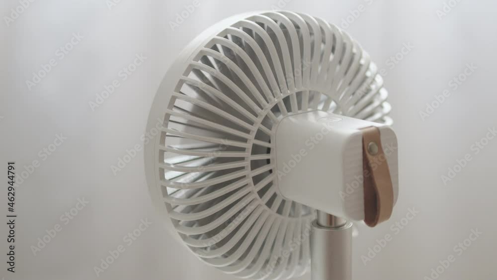 Modern white portable electric fan on light white background. Hanging matte white tulle. Back view Modern white portable electric fan on light white background. Hanging matte white tulle. Back view