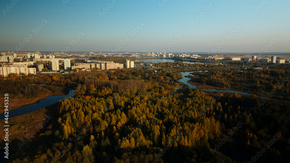 Flight over the autumn park. Trees with yellow autumn leaves are visible. On the horizon there is a blue sky and city houses. The park river is visible. Aerial photography.