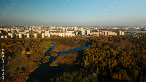 Flight over the autumn park. Trees with yellow autumn leaves are visible. On the horizon there is a blue sky and city houses. The park river is visible. Aerial photography. © f2014vad