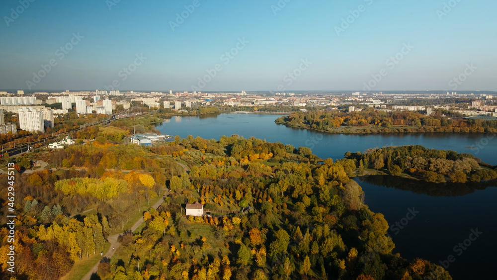 Flight over the autumn park. Trees with yellow autumn leaves are visible. On the horizon there is a blue sky and city houses. The park lake is visible. Aerial photography.