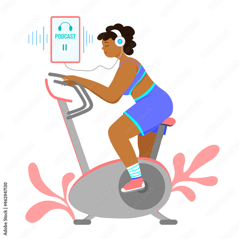 Fototapeta premium Dark - skinned girl listens to a podcast on a mobile and is engaged on an exercise bike