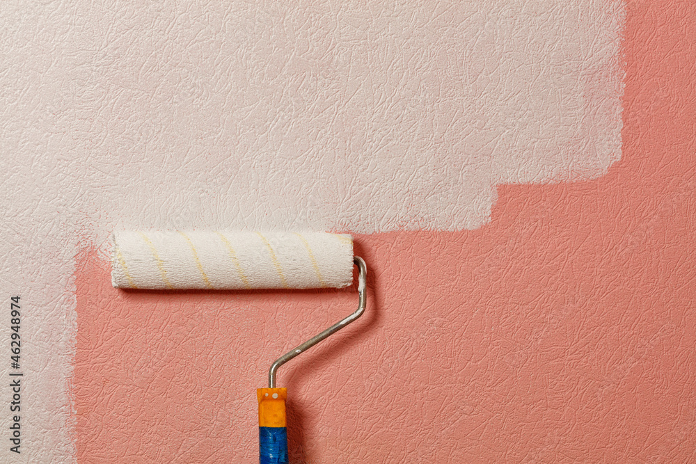 Obraz premium Paint roller paints pink wallpaper on the wall with white paint, copy space.
