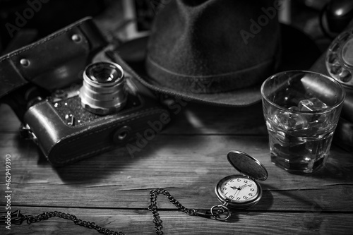 Old vintage cinematic noir scene, detective's desk with a hat, telephone, camera, portable cassette recorder, and whisky