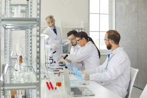 Group of different medical scientists work together in a modern scientific laboratory. Senior scientist and his young assistants are working together to develop a new drug. Medicine concept.